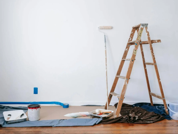 Interior decorating in progress with paint tin, brushes and masking tape on wooden floor
