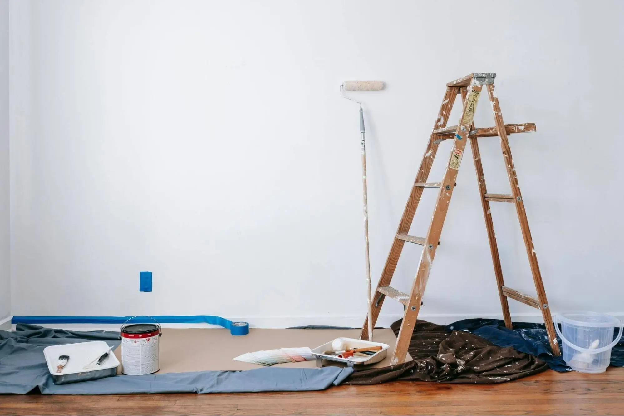 Interior decorating in progress with paint tin, brushes and masking tape on wooden floor