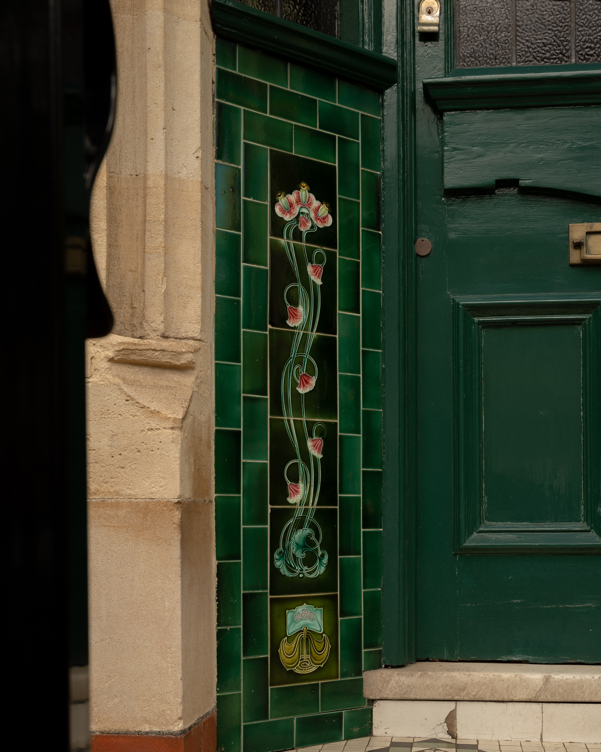 Green Victorian front door with floral tiled porch panel on a period house