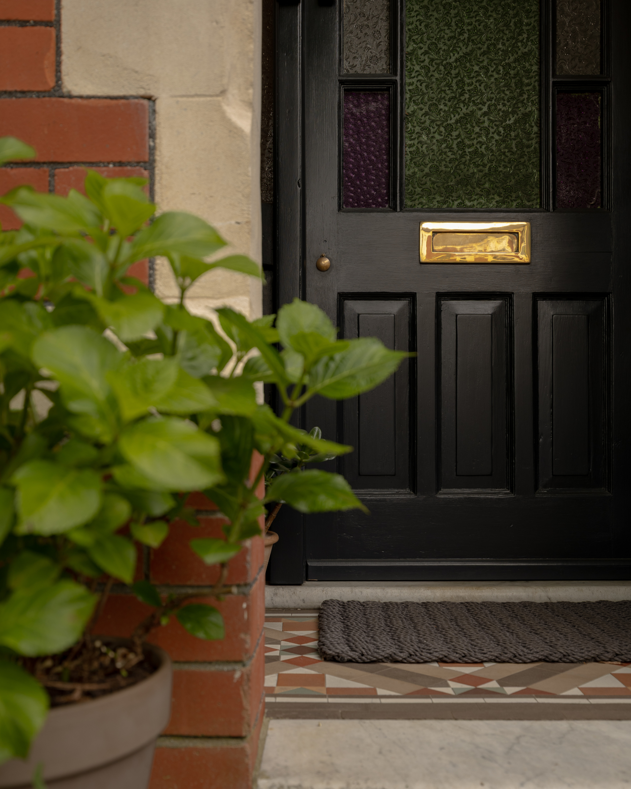 Black front door with brass letterbox and coloured glass panels on a red brick terrace in Roath